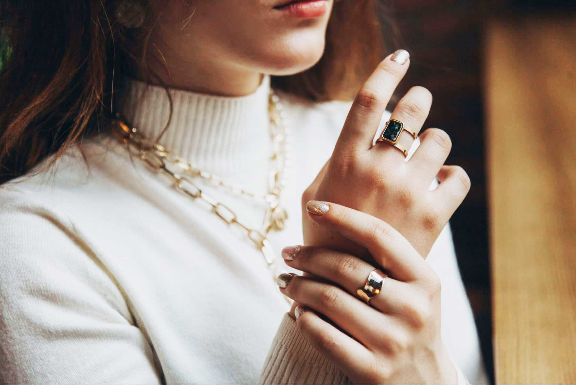 Manos con anillos y collar artesanal de Joyería Sarang en fondo cálido